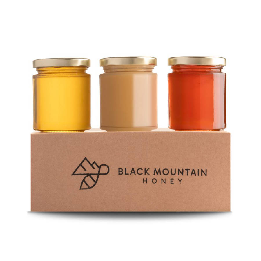 Three jars of honey in clear jars on a black mountain honey branded presentation box